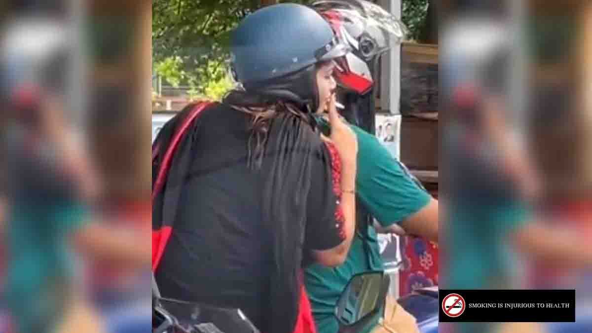 Indian woman sitting on a motorbike behind her husband, smoking a cigarette and handing it to him at a traffic signal, viral video moment