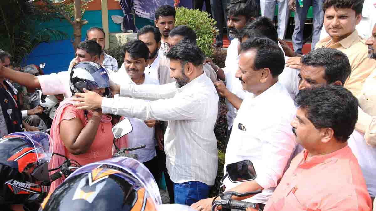MP Sudhakar distributing free helmets to two-wheeler riders during a road safety awareness program in Gudibande, Chikkaballapur district